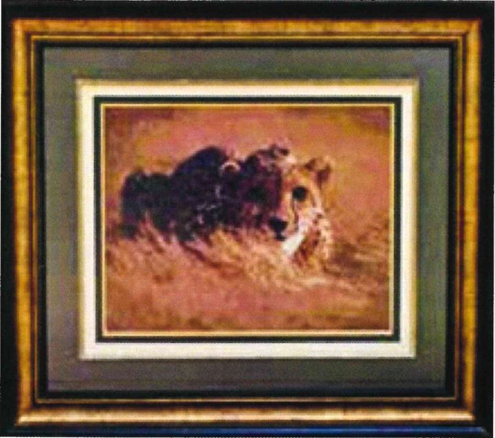 Cross-stitch artwork of a cheetah crouching low in dry grass, stitched in warm browns, in a gold frame with a green mat.