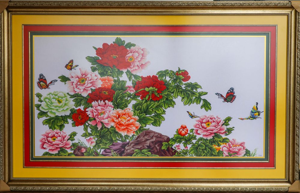 Long framed cross stitch of red and pink peonies with butterflies.