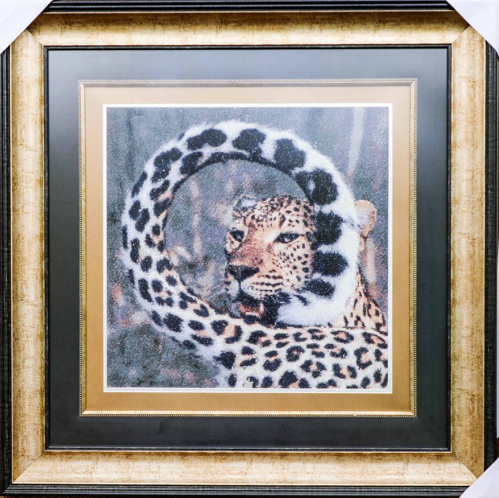 Framed cross stitch of a leopard, its spotted tail curled in a ring around its head.