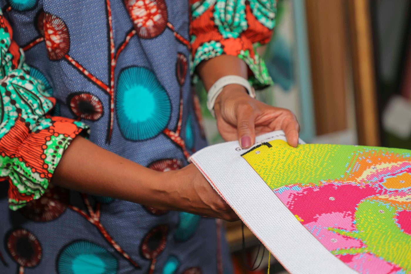 Hands holding up a finished length of brightly coloured cross stitch, the white evenweave border still visible.