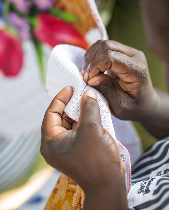 Close-up of an artisan's hands drawing thread through evenweave fabric with a needle.